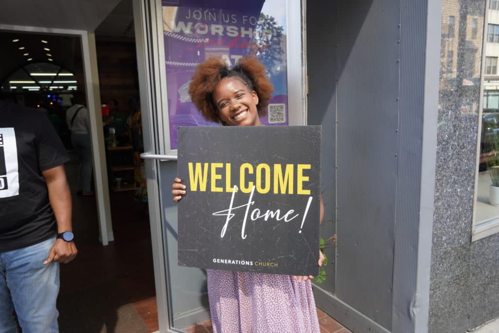 A young lady holding a welcome sign for Generations Church guests